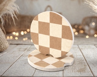 May include: Two circular car coasters featuring a tan and cream checkered pattern. Each coaster has a small semi-circular notch cut out from the edge. The coasters are made of a flat, matte material and are stacked with one standing upright.