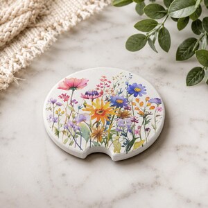 K&ouml;nnte beinhalten: Ein runder, wei&szlig;er Auto-Getr&auml;nkehalter-Untersetzer mit einer farbenfrohen Aquarellillustration verschiedener Wildblumen in Rosa, Gelb und Blau. Der Untersetzer verf&uuml;gt &uuml;ber eine kleine halbkreisf&ouml;rmige Aussparung am unteren Rand.
