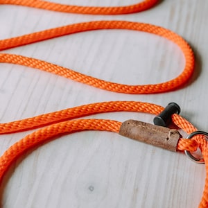 May include: Orange rope dog leash with a brown leather handle and a metal ring.