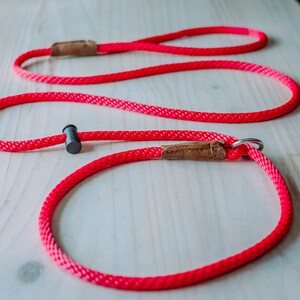 May include: A bright pink dog leash with a brown leather handle and a black metal clip. The leash is made of a thick, durable rope.