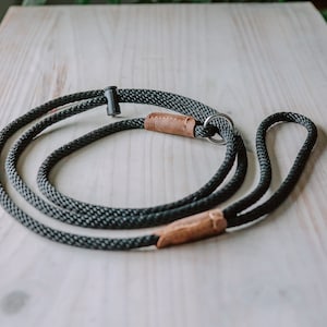 May include: A black and brown rope dog leash with a metal ring and a leather accent.