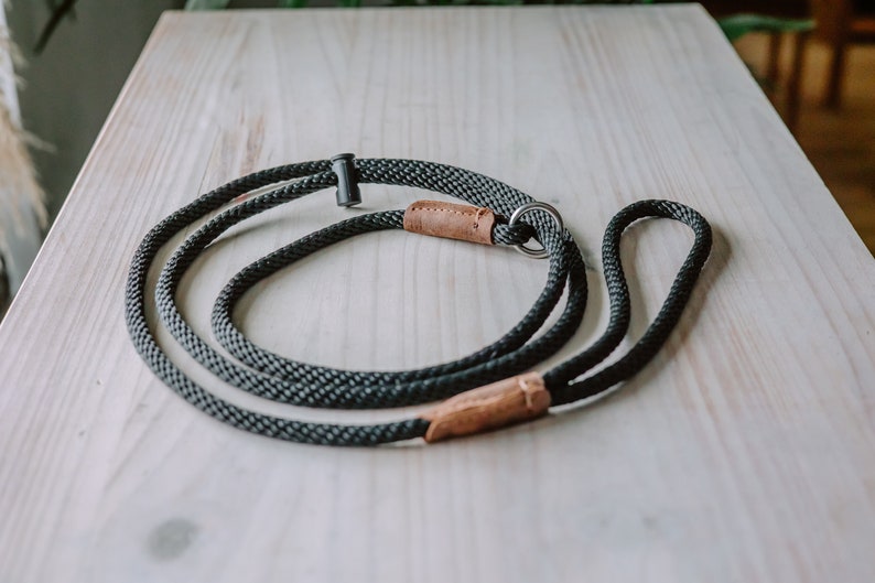 May include: A black and brown rope dog leash with a metal ring and a leather accent.