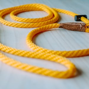 May include: A yellow rope dog leash with a brown leather handle and a silver metal clip.