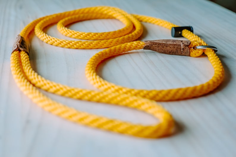 May include: A yellow rope dog leash with a brown leather handle and a silver metal clip.