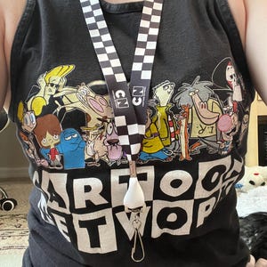 May include: Black tank top featuring a Cartoon Network graphic with various cartoon characters. A lanyard with a black and white checkered pattern and "CN" text is around the neck. A white whistle is attached to the lanyard.