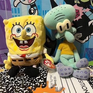 May include: Two plush toys of SpongeBob SquarePants and Squidward Tentacles from the animated series, SpongeBob SquarePants. SpongeBob is yellow with a brown tie and Squidward is teal. The toys are on a composition notebook and a Nickelodeon-themed background.