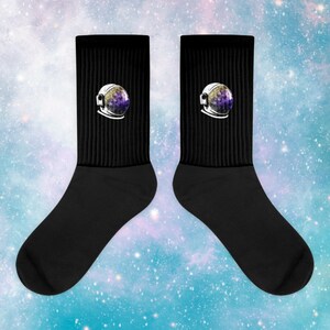 May include: A pair of black crew socks with a galaxy astronaut helmet design. The helmet is white with a purple and yellow galaxy inside.
