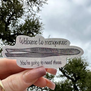 A hand drawn water resistant sticker featuring a pair of tweezers illustrated in a simple, playful style, along with the text “Welcome to menopause, you’re going to need these.” The artwork uses clean lines and a lighthearted tone to emphasize the humorous message.
