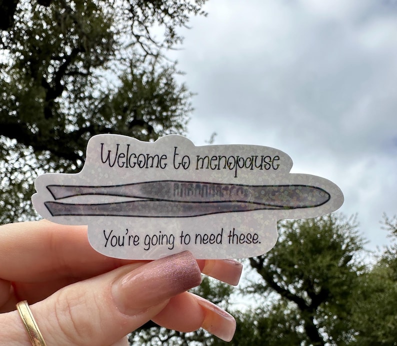 A hand drawn water resistant sticker featuring a pair of tweezers illustrated in a simple, playful style, along with the text “Welcome to menopause, you’re going to need these.” The artwork uses clean lines and a lighthearted tone to emphasize the humorous message.