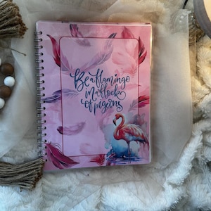May include: A pink spiral bound notebook with a watercolor design of feathers and a flamingo. The notebook has the text "Be a flamingo in a flock of pigeons" on the front cover.