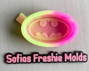 May include: A pink and yellow silicone mold shaped like a Batman logo. The mold is designed for making resin crafts. The text "Sofias Freshie Molds" is visible below the mold.