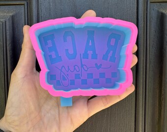 May include: Pink and blue silicone mold with the word "RACE" in white letters and the word "day" in cursive with a small heart above it. The mold has a checkered pattern at the bottom.