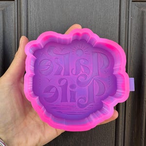 May include: Purple silicone mold with a raised design of the words "Lake Life" in a stylized font. The mold has a pink rim.