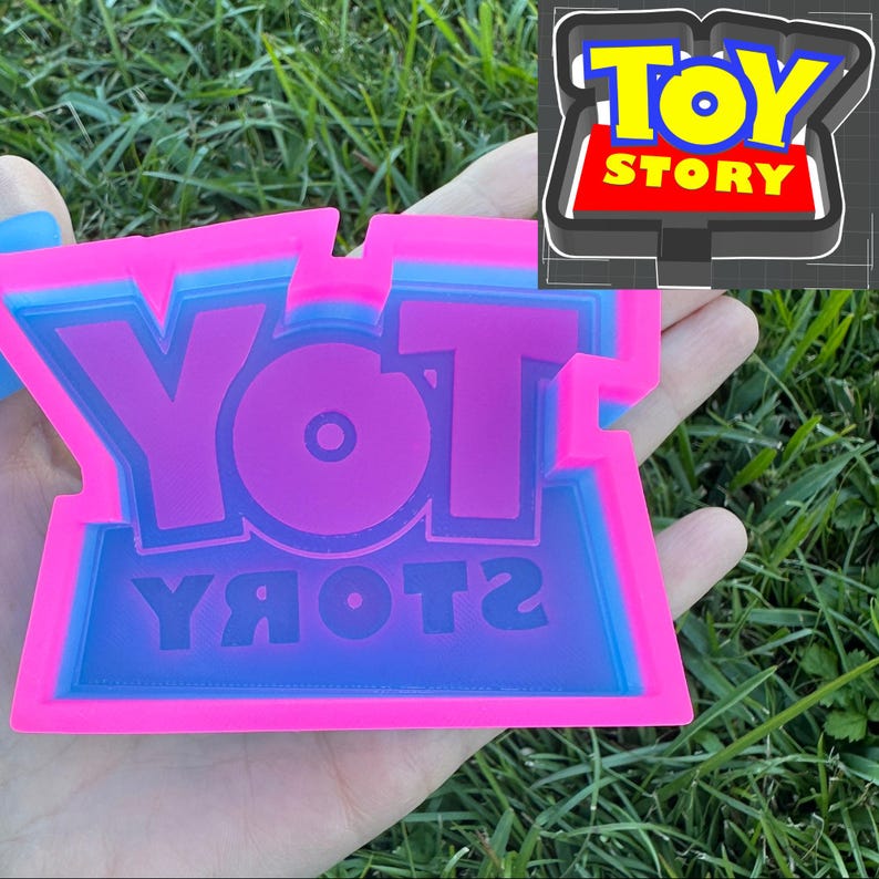 May include: A pink and blue silicone mold with the words "YOT YЯOЯ2" in a reversed font. The mold is designed to create a replica of the Toy Story logo.