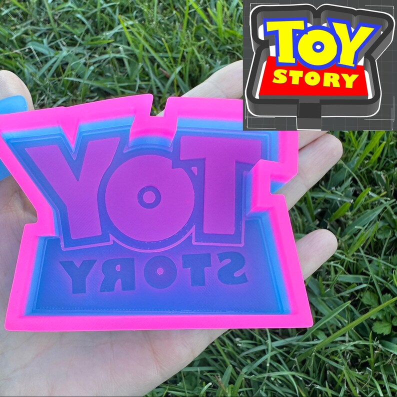 May include: A pink and blue silicone mold with the words "YOT YЯOTOЯ" in a reversed font. The mold is designed to create a replica of the Toy Story logo.