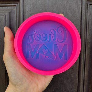 May include: Pink silicone mold with a purple interior. The mold has the words "Cheer Mom" and a cheerleader megaphone with a heart on it.