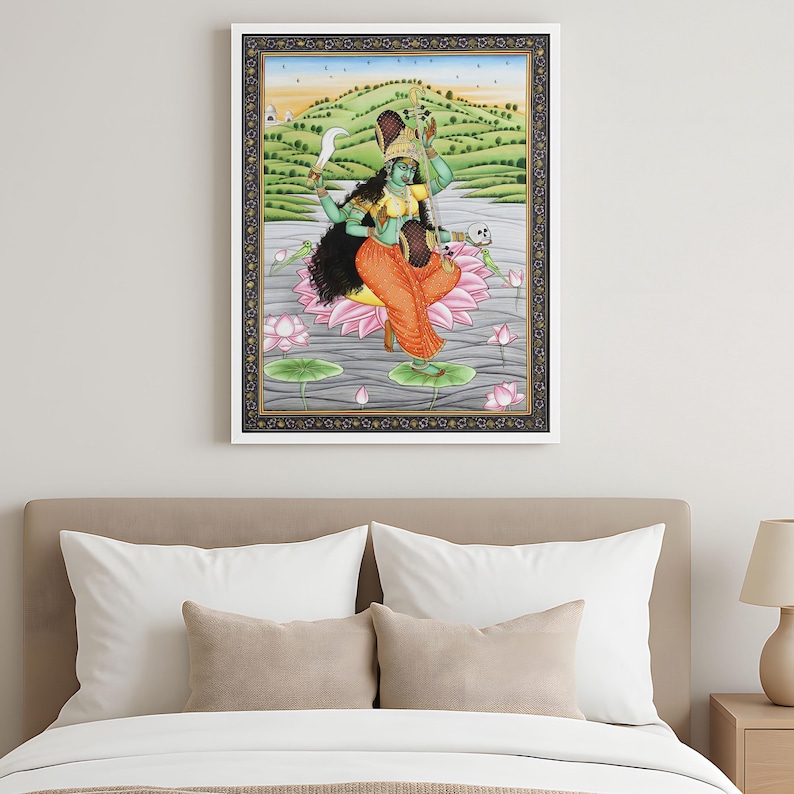 K&ouml;nnte beinhalten: Gerahmtes Kunstwerk, das eine Gottheit mit gr&uuml;ner Haut zeigt, die ein gelbes Oberteil und eine orangefarbene Hose tr&auml;gt und auf einer rosa Lotusblume sitzt. Der Hintergrund zeigt eine Landschaft mit gr&uuml;nen H&uuml;geln und blauem Himmel. Das Kunstwerk ist in einem wei&szlig;en und goldenen Rahmen gerahmt.