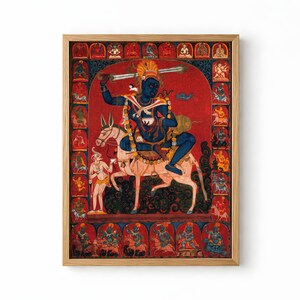 Op de afbeelding: Een ingelijste rechthoekige print met een centrale blauwe godheid die een zwaard en kom vasthoudt terwijl deze op een lichtgekleurd dier rijdt. De scène is tegen een dieprode achtergrond geplaatst, omringd door kleinere, kleurrijke illustraties.