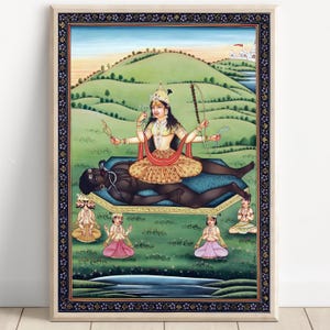 Puede incluir: Pintura enmarcada y colorida que representa una deidad con múltiples brazos, sentada sobre una figura oscura. El fondo muestra un paisaje verde con colinas, un cielo azul y pequeñas figuras. La obra de arte tiene un borde detallado.