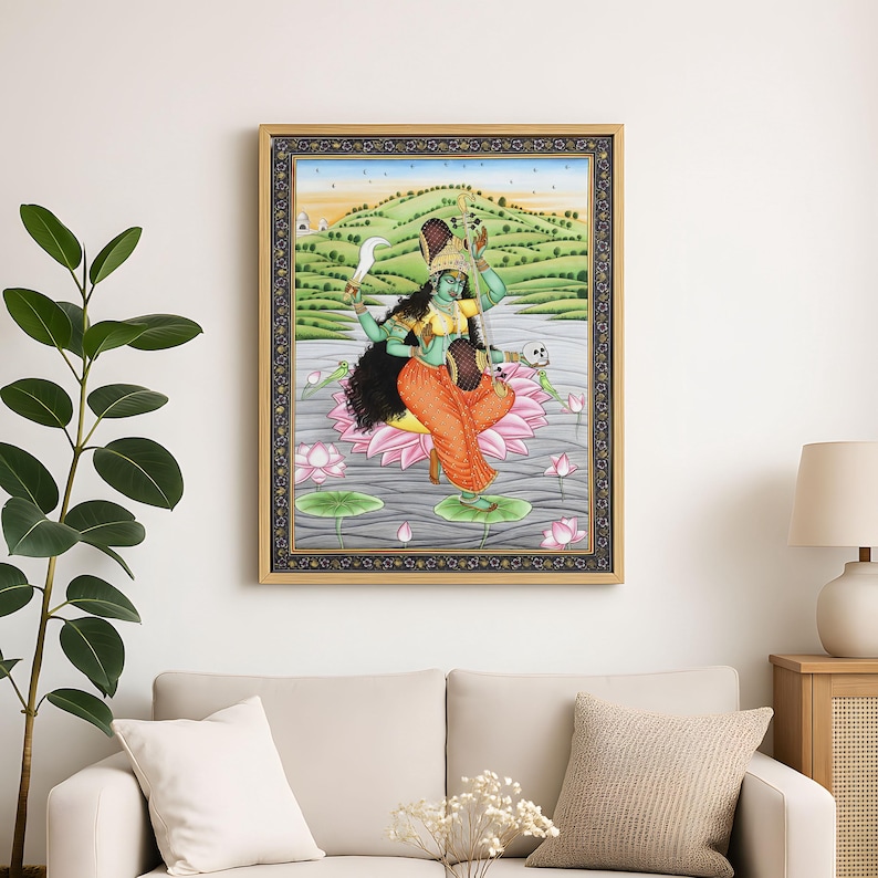K&ouml;nnte beinhalten: Gerahmtes Kunstwerk, das eine Gottheit mit gr&uuml;ner Haut, orangefarbener Kleidung und mehreren Armen zeigt. Die Gottheit sitzt auf einer rosa Lotusblume im Wasser, mit einer Landschaft im Hintergrund. Das Kunstwerk ist in einem goldenen Rahmen.