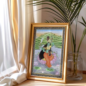 K&ouml;nnte beinhalten: Ein gerahmtes Kunstwerk, das eine t&uuml;rkisfarbene Gottheit mit mehreren Armen zeigt, die ein Schwert und andere Gegenst&auml;nde h&auml;lt und auf einer Lotusblume steht. Das Kunstwerk ist vor dem Hintergrund einer Landschaft mit einem Fluss und H&uuml;geln in einem goldfarbenen Rahmen.