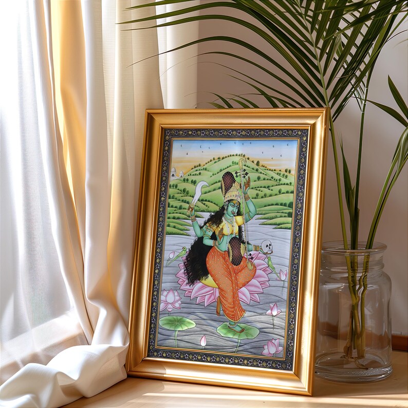 K&ouml;nnte beinhalten: Ein gerahmtes Kunstwerk, das eine t&uuml;rkisfarbene Gottheit mit mehreren Armen zeigt, die ein Schwert und andere Gegenst&auml;nde h&auml;lt und auf einer Lotusblume steht. Das Kunstwerk ist vor dem Hintergrund einer Landschaft mit einem Fluss und H&uuml;geln in einem goldfarbenen Rahmen.