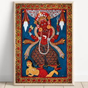 Può includere: Opera d'arte incorniciata raffigurante una divinità dalla carnagione rossa, ornata da gioielli intricati e un copricapo. La figura è ambientata su uno sfondo blu, con un bordo decorativo rosso e oro. L'opera presenta elementi artistici tradizionali.