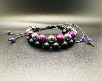 May include: A double-strand bracelet featuring alternating matte black beads, metallic silver-toned beads, and vibrant magenta-purple beads. The beads are strung on black cord with adjustable pull-ties finished with small purple accent beads.