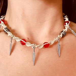 May include: A white macrame choker necklace with red glass beads and silver feather charms.