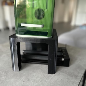 Könnte beinhalten: Ein schwarzer Plastikständer mit einem durchsichtigen Glasbehälter oben drauf. Der Behälter ist mit einer grünen Flüssigkeit gefüllt und hat einen weißen Plastikgriff.