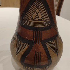 Peut inclure: Un vase en céramique brun avec un motif géométrique en noir et blanc. Le vase a une base large et un col étroit.