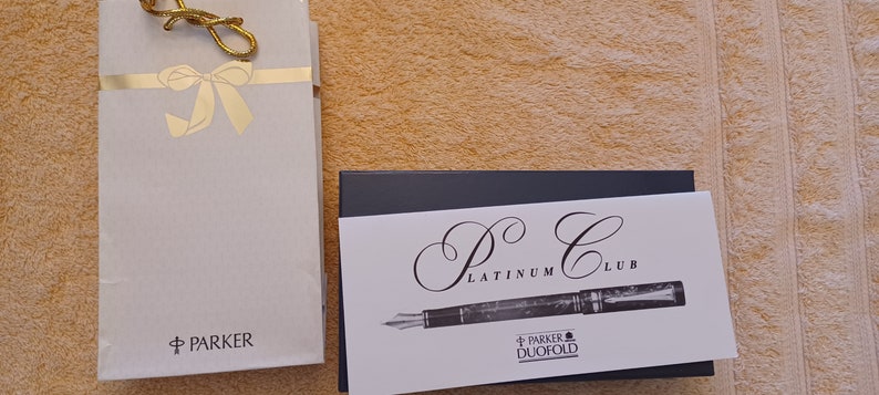 Puede incluir: Un bol&iacute;grafo fuente Parker Duofold Platinum Club en una caja negra con una tarjeta blanca que dice "P.C. Platinum Club" y "Parker Duofold".