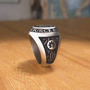 May include: A silver ring with a black gear design and the words "SOURCE HAB" engraved on the band.