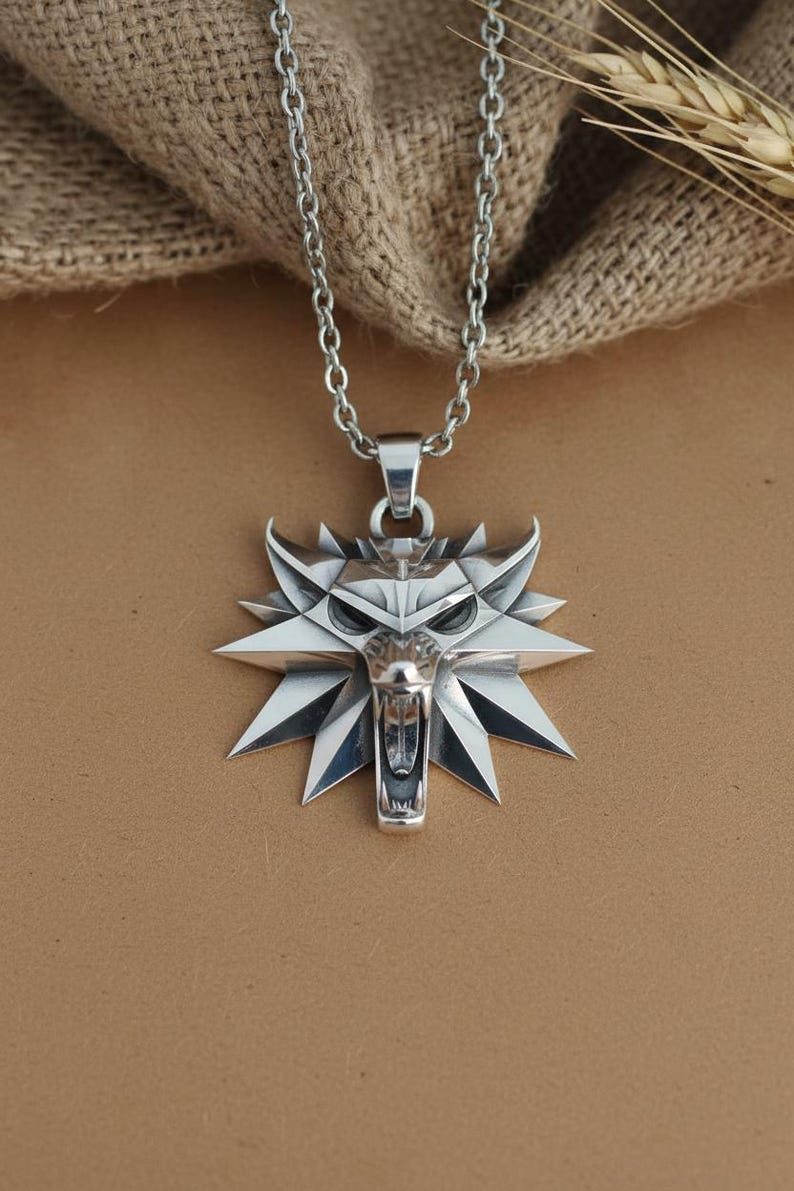 May include: A silver-colored pendant necklace featuring a wolf head design. The pendant has a detailed, angular wolf head with an open mouth and sharp features. The necklace chain is also silver and hangs against a neutral background.
