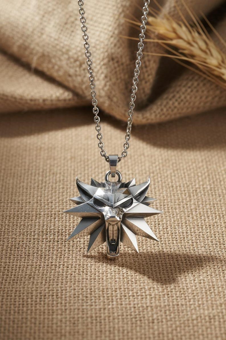 May include: Silver-colored pendant necklace featuring a wolf head emblem with a geometric design. The pendant is suspended from a delicate chain. The necklace is displayed against a neutral, textured background.
