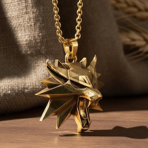 May include: A gold-colored pendant necklace featuring a stylized wolf head with sharp angles and open mouth. The pendant hangs from a delicate chain. The background includes a wooden surface and a textured fabric.
