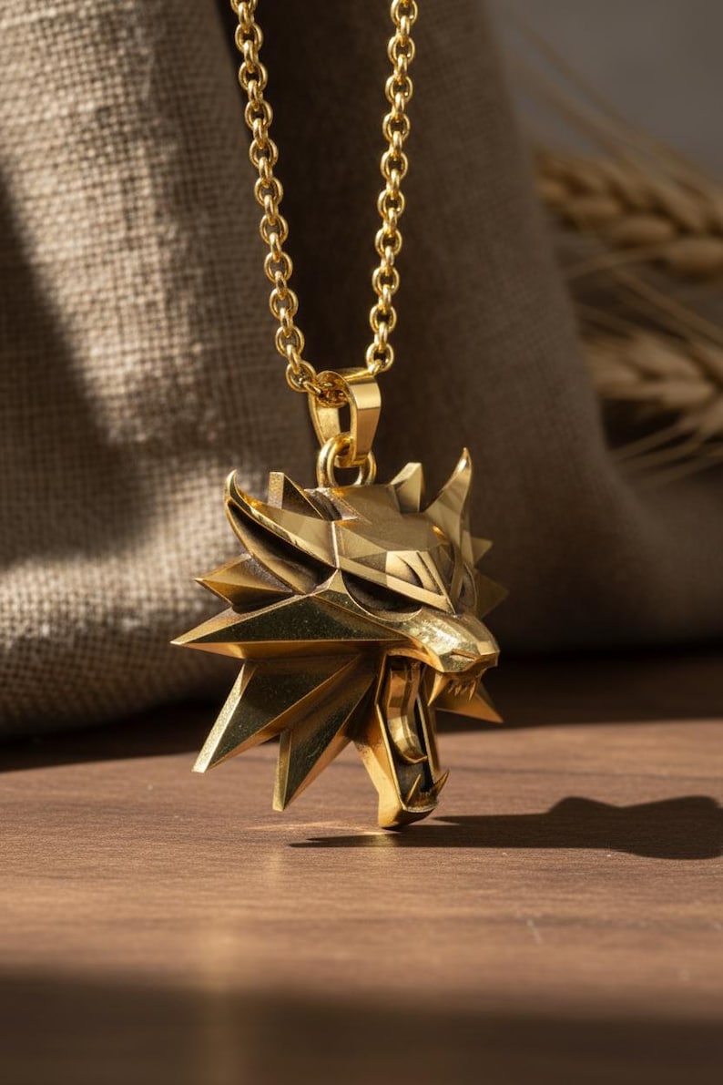 May include: A gold-colored pendant necklace featuring a stylized wolf head with sharp angles and open mouth. The pendant hangs from a delicate chain. The background includes a wooden surface and a textured fabric.