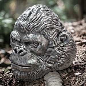 Könnte beinhalten: Eine silberfarbene Gorillakopfskulptur mit detailliertem Fell und Gesichtszügen. Die Skulptur steht auf einer braunen, strukturierten Oberfläche.