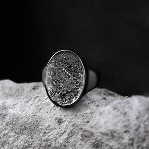 Könnte beinhalten: Ein schwarzer Siegelring mit einem strukturierten ovalen Stein.