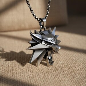 May include: Silver-toned pendant necklace featuring a stylized wolf head with an open mouth and sharp teeth. The pendant is suspended from a matching chain. The design has a geometric, angular aesthetic, and the necklace is likely made of metal.