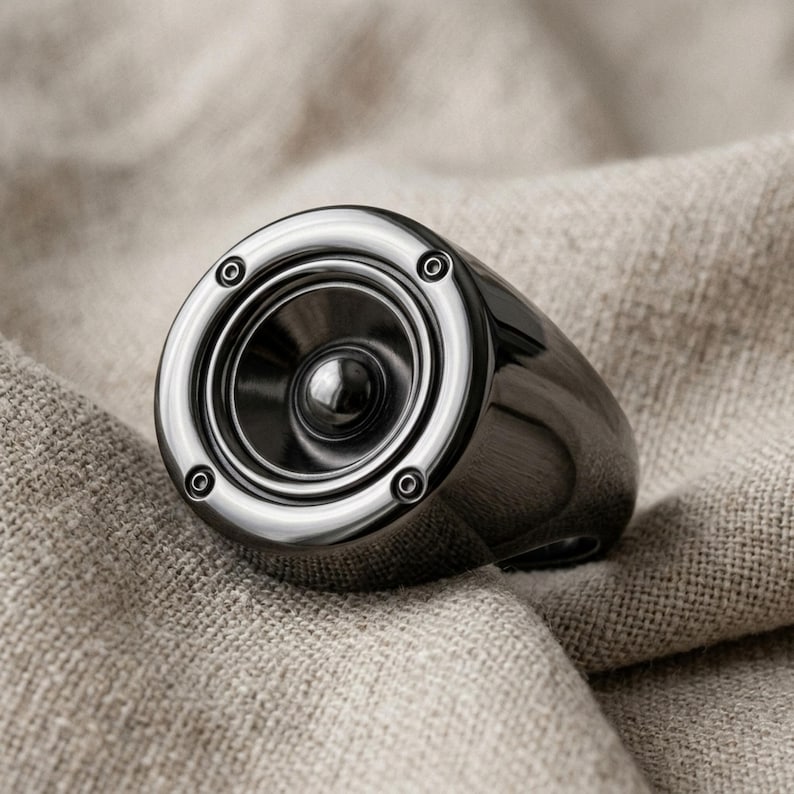 A close-up image of a black speaker with a reflective surface, resting on a beige fabric background.
