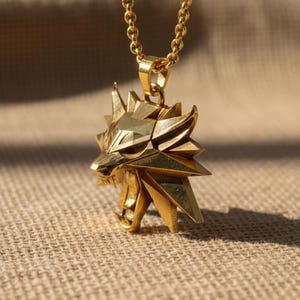 May include: A gold-colored pendant necklace featuring a stylized wolf head. The pendant has a geometric design with sharp angles and is suspended from a matching chain. The necklace is displayed against a neutral background.