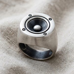 A silver ring with a unique design resembling a speaker or audio equipment.