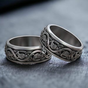 Puede incluir: Dos anillos de plata con intrincados diseños de nudos celtas. Los anillos están apilados uno encima del otro, mostrando los patrones detallados.