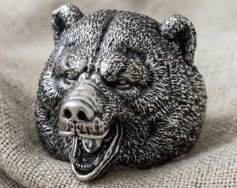May include: A silver-toned ring featuring a highly detailed, three-dimensional bear head. The bear has a textured fur finish, visible eyes, and an open mouth revealing teeth. The metal has a darkened, oxidized appearance in the recessed areas.