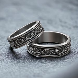 May include: Two silver wedding bands with an intricate floral design.