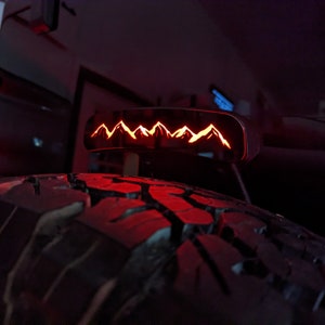 May include: A black metal rear window mount with a red LED light that displays a mountain range silhouette.