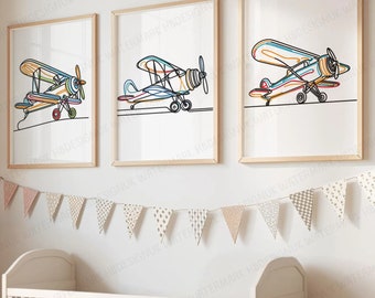 Pode incluir: Três quadros de parede emoldurados com desenhos de linha contínua de aviões antigos em cores vibrantes. Cada impressão exibe um design único de biplano com contornos vermelhos, azuis, laranja e amarelos sobre um fundo branco liso.
