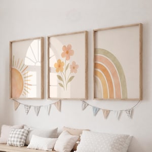May include: Three framed wall art prints featuring a sun, a flower bouquet, and a rainbow in muted earth tones. The prints are displayed in light wood frames above a storage unit with white bins and various patterned throw pillows.
