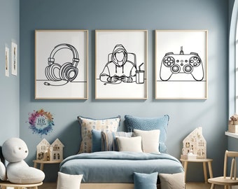 Puede incluir: Tres impresiones en blanco y negro de arte de línea que representan a un jugador con auriculares, un jugador jugando a un videojuego y un mando de videojuego. Las impresiones están enmarcadas y colgadas en una pared azul claro sobre una cama azul con almohadas blancas y grises.